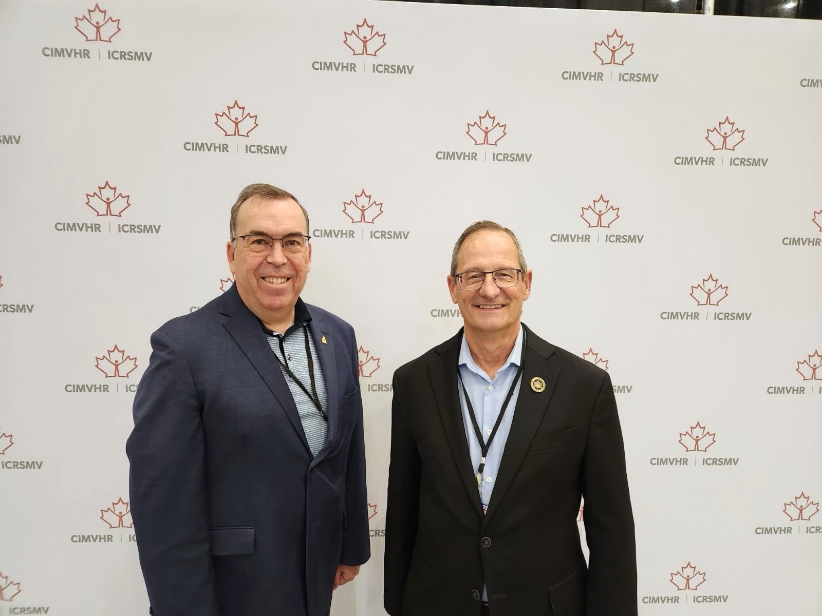 Deputy Chairperson Jacques Bouchard and Board Member Patrice Carrière standing in front of a white Banner with the logo for the Canadian Institute for Military and Veteran Health Research
