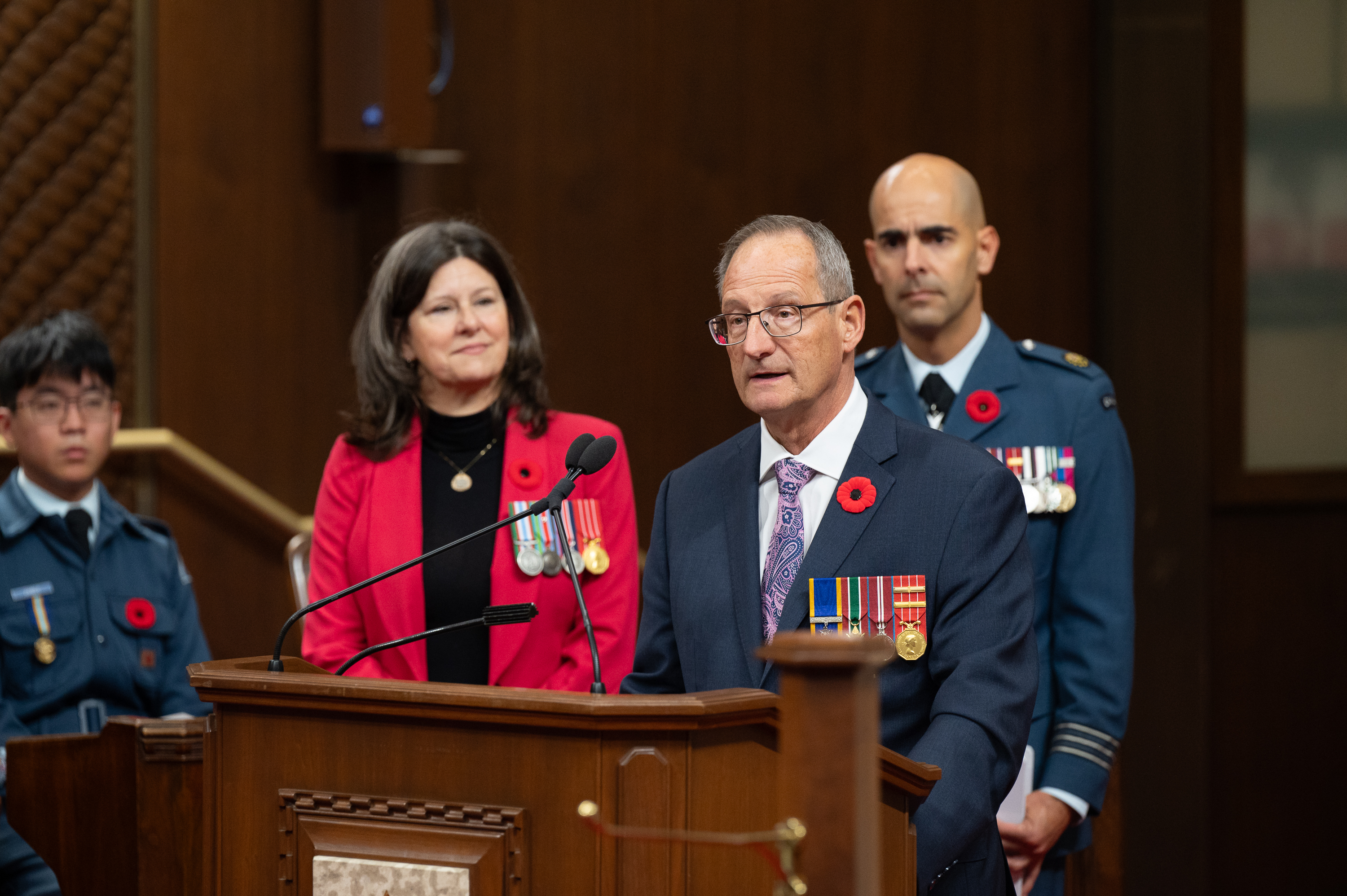 Board Deputy Chairperson Jacques Bouchard standing at a podium with a microphone reciting the Act of Remembrance at the 2024 Senate Ceremony in Ottawa during Veterans’ Week.