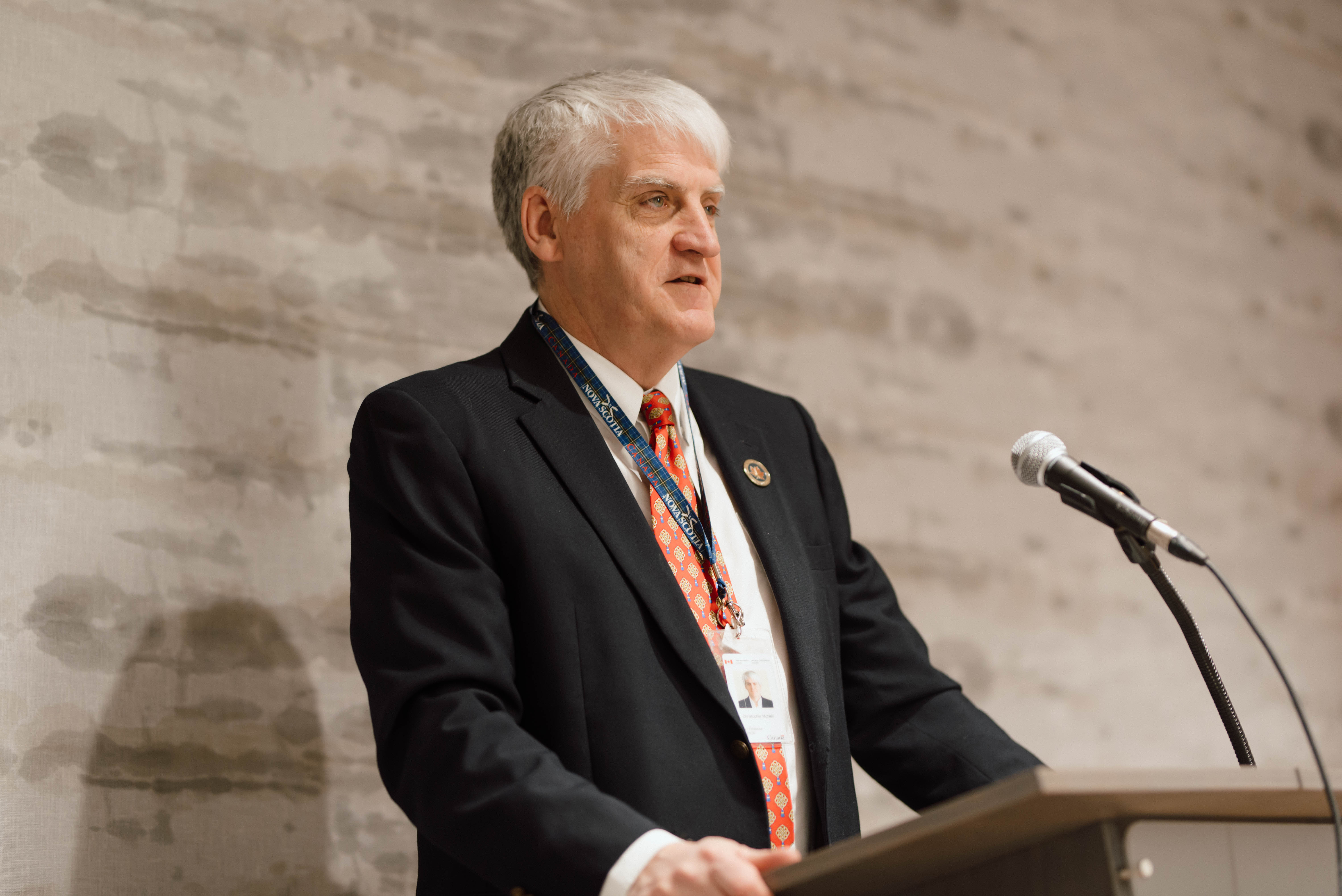 Board Chairperson Christopher J. McNeil speaking at a podium.